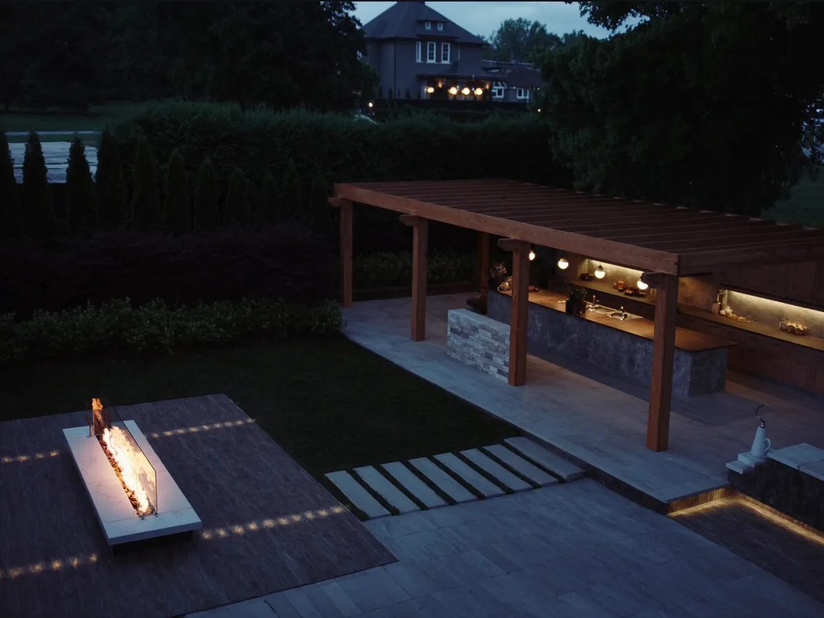 Interlocking patio and outdoor kitchen in the Kingsway, Etobicoke — cedar pergola and linear fire feature at dusk